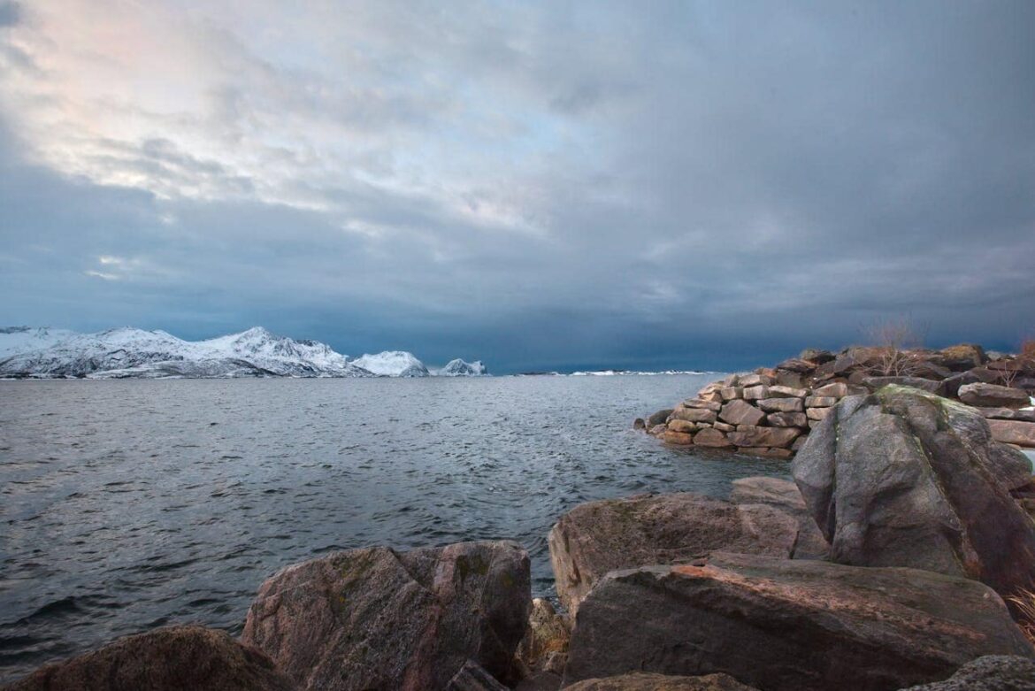 Panorama côtier avec rochers au premier plan et montagnes enneigées au loin pour visiter Tromsø en hiver