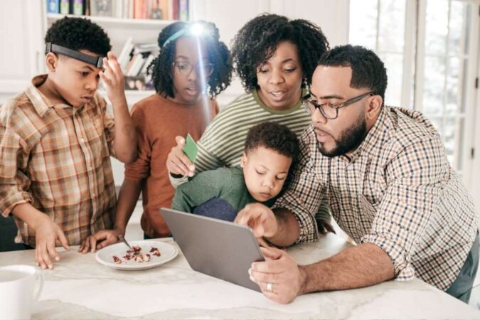 Une famille utilisant une tablette numérique pour planifier ensemble leur prochain voyage organisé à la maison.