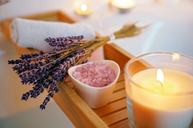 Un plateau en bois présente des bougies allumées et des brins de lavande pour illustrer les rituels de bien-être à la maison.
